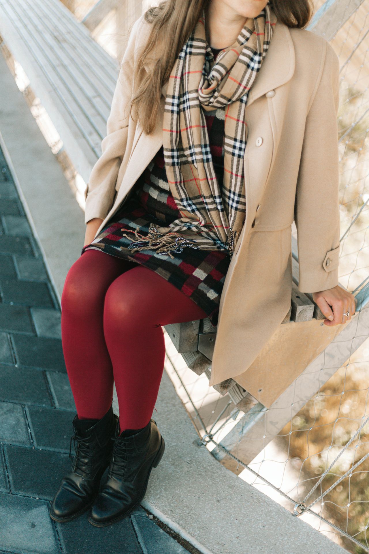 Woman wearing a plaid blanket scarf with a beige coat and ankle boots