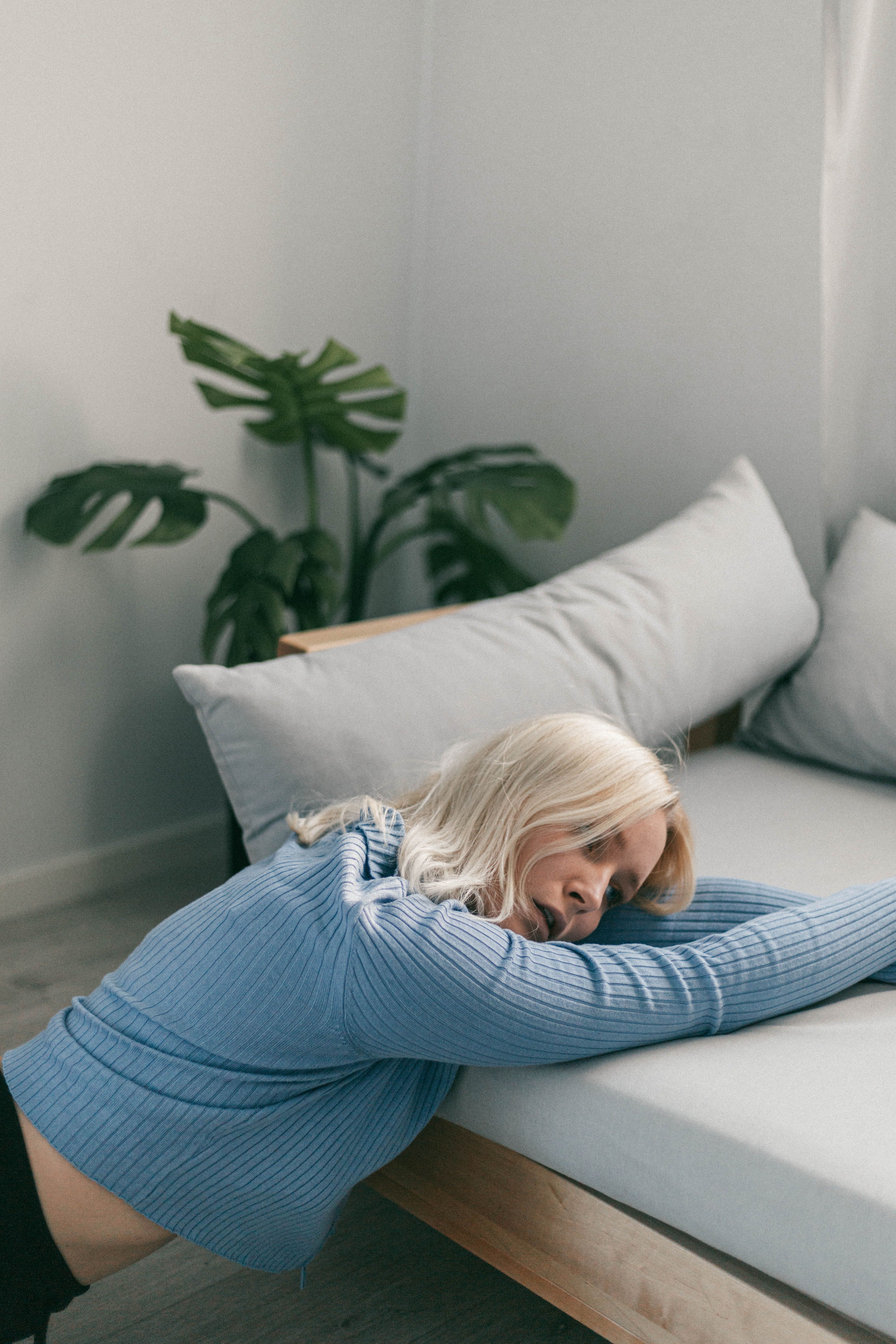 A young woman in a blue sweater stretches on a modern sofa in a cozy living room.