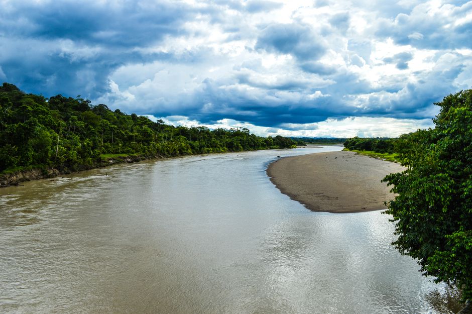 A vibrant landscape of a river winding through lush greenery under dramatic skies in Puerto Nuevo, Chocó, Colombia.