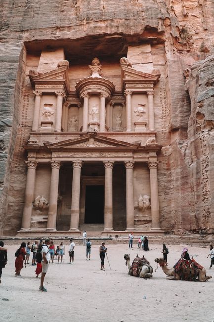 The iconic Treasury at Petra, Jordan with tourists and camels in front.