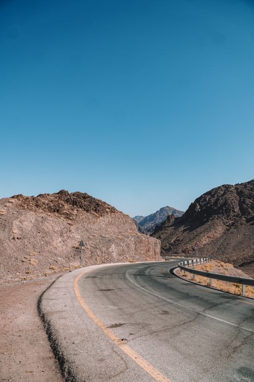 Free A winding road through desert mountains with a clear blue sky, perfect for travel and outdoor themes. Stock Photo