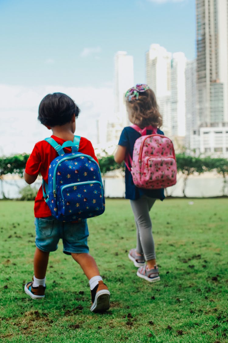 Boy And Girl With Backpacks Walking On Grass