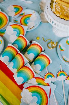 Vibrant and joyful rainbow-themed party decor with plates, cups, and napkins on a light blue tablecloth.