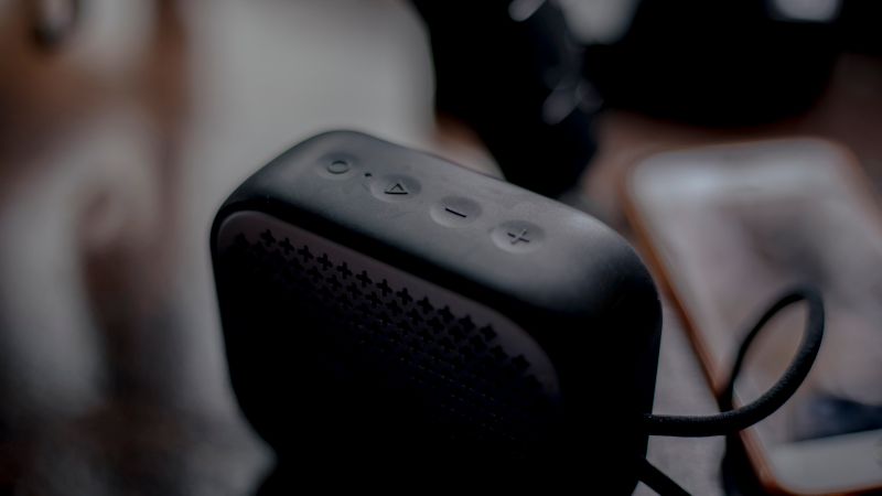 A sleek portable Bluetooth speaker next to a smartphone on a wooden table, emphasizing modern technology.