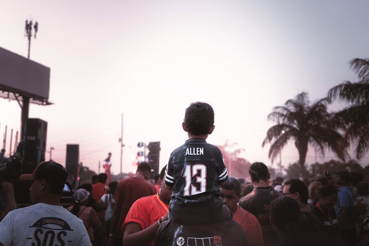 Child Sitting On Persons Back In A Crowd At A Festival 