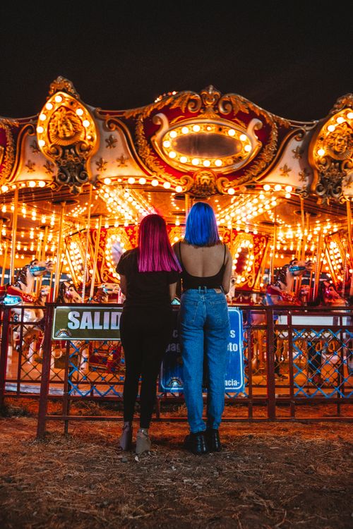 Free Two women with vibrant hair enjoy illuminated carousel rides at night. Stock Photo