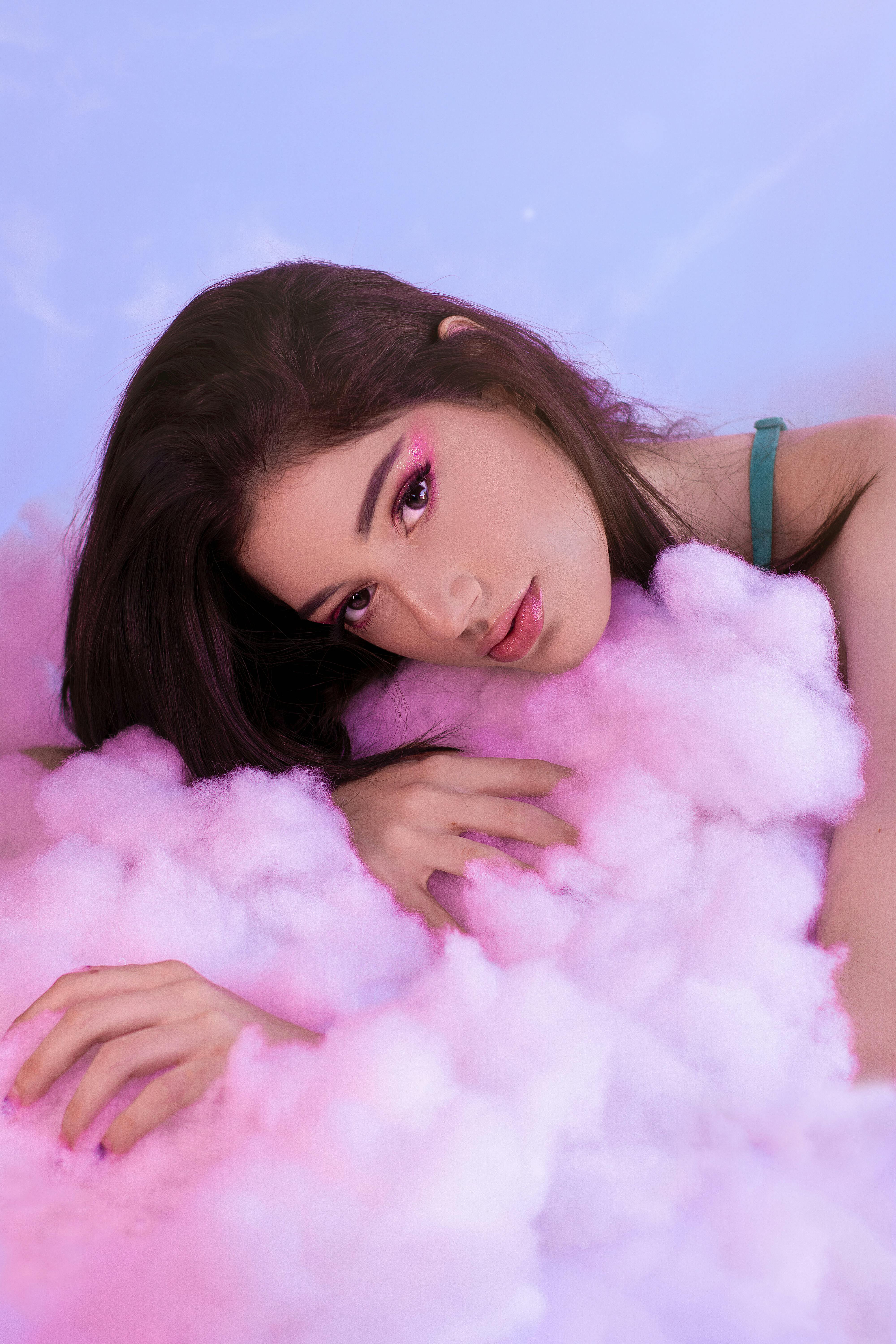 Ethereal portrait of a woman resting in fluffy pink cotton against a pastel background.