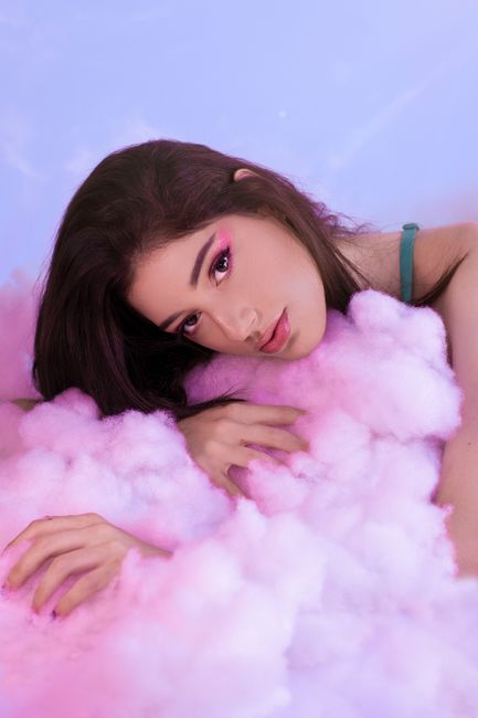Ethereal portrait of a woman resting in fluffy pink cotton against a pastel background.
