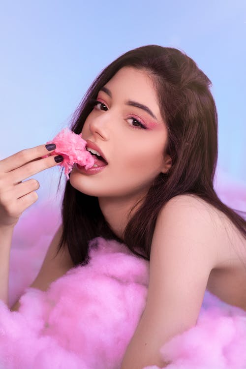 Young Woman Lying on Cotton Candy and Eating a Piece of It 