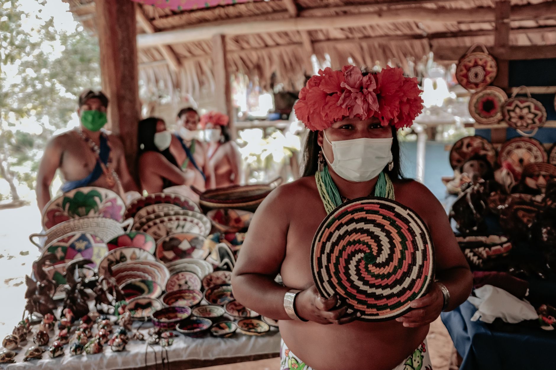 Indigenous artisan at market with colorful woven basket and pottery. Cultural display.