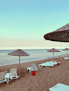 Peaceful beach scene with empty sun loungers and straw umbrellas by the shore.