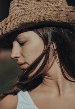 Side profile of a woman with eyes closed wearing a cowboy hat outdoors.