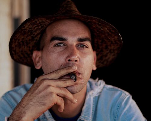 Free Close-up portrait of a man wearing a straw hat and smoking a cigar, showcasing a thoughtful expression. Stock Photo