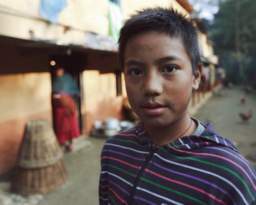 A Boy in Colorful Striped Jacket Looking at the Camera