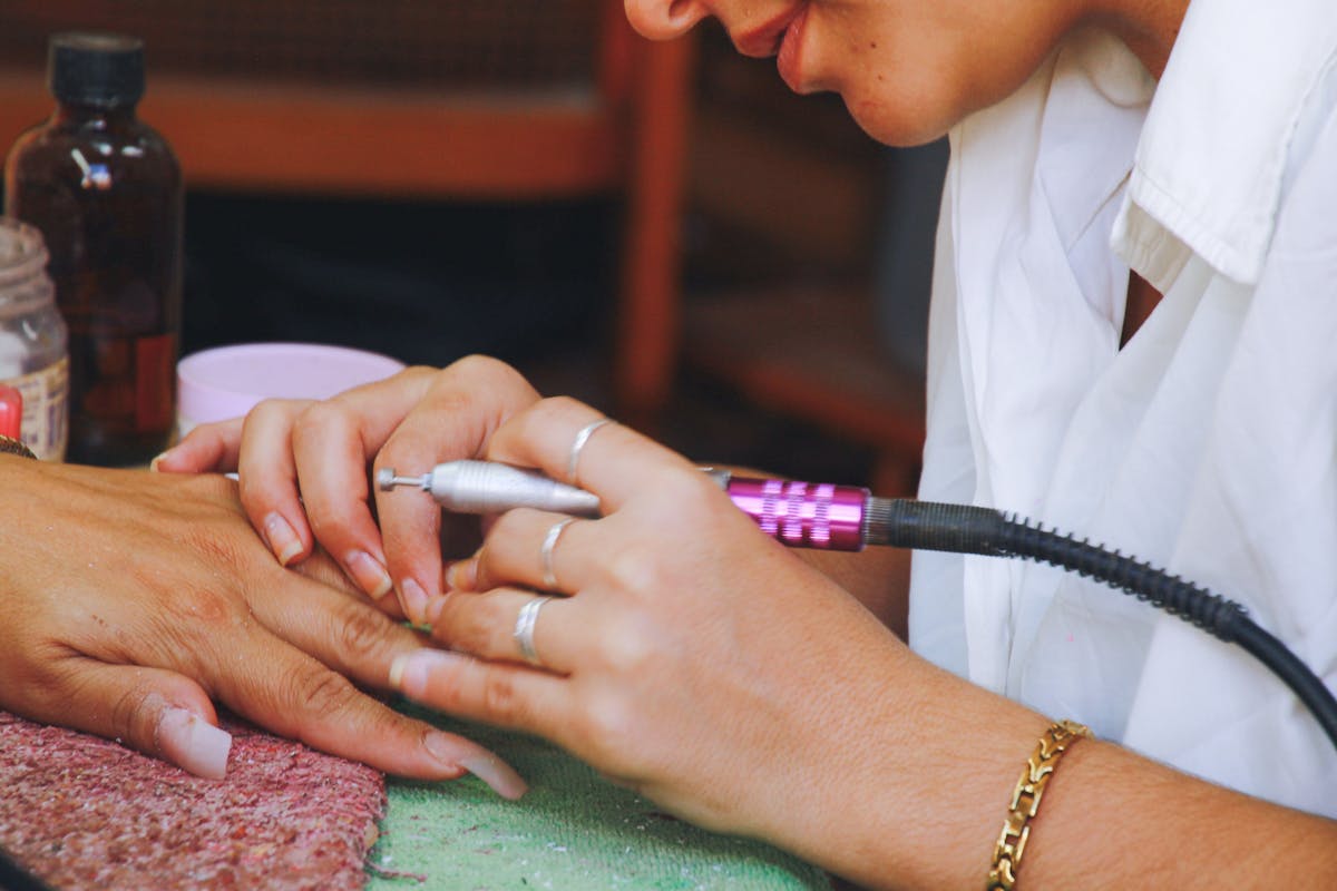 Close-up image of a nail technician using an electric file on a client's nails during a manicure session.