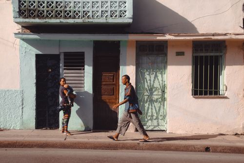 Free A man passing by a mother holding a child on a sunny city street. Stock Photo