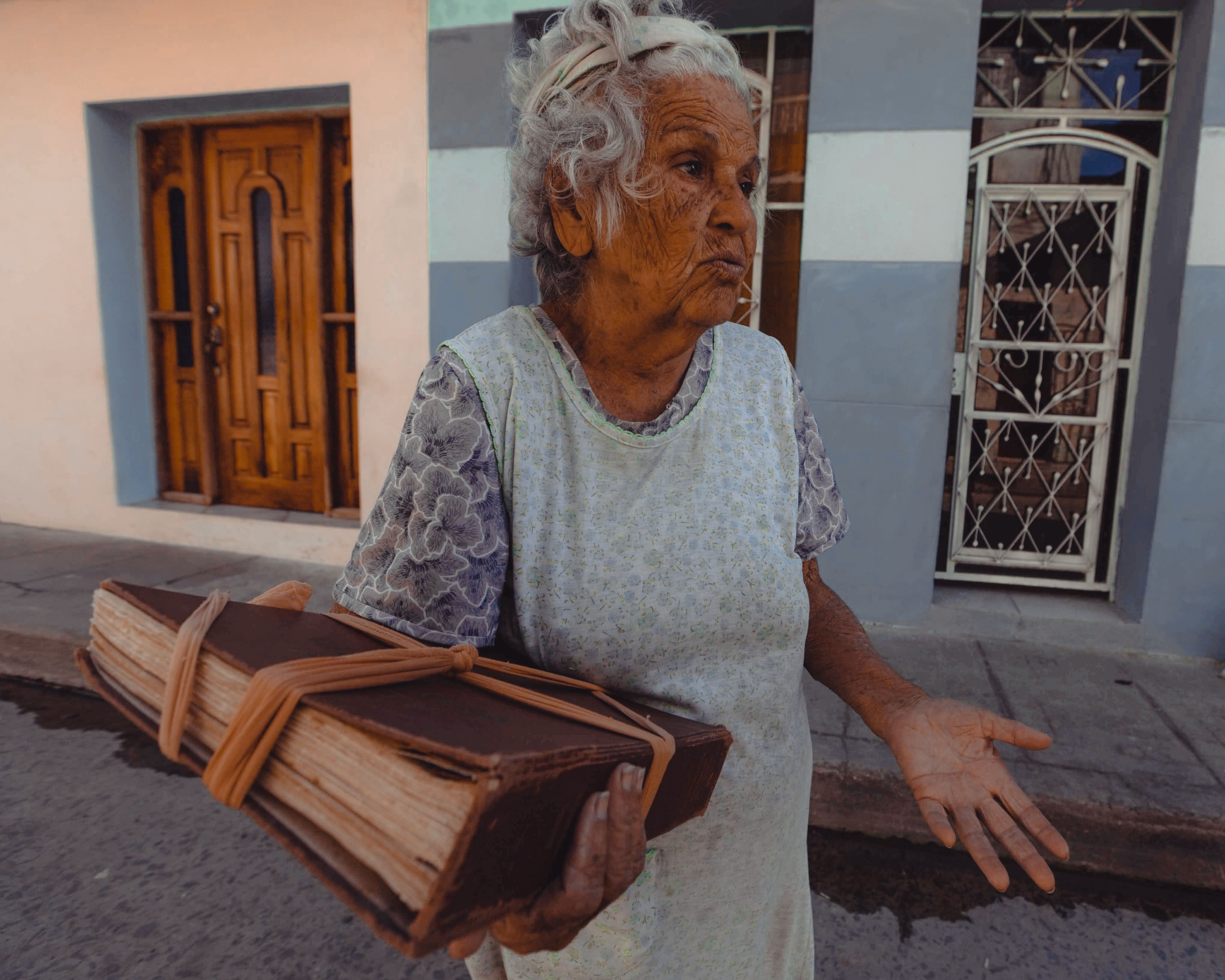 Fotomural Una mujer anciana está de pie en la calle sosteniendo un gran libro histórico, transmitiendo sabiduría y relatos.