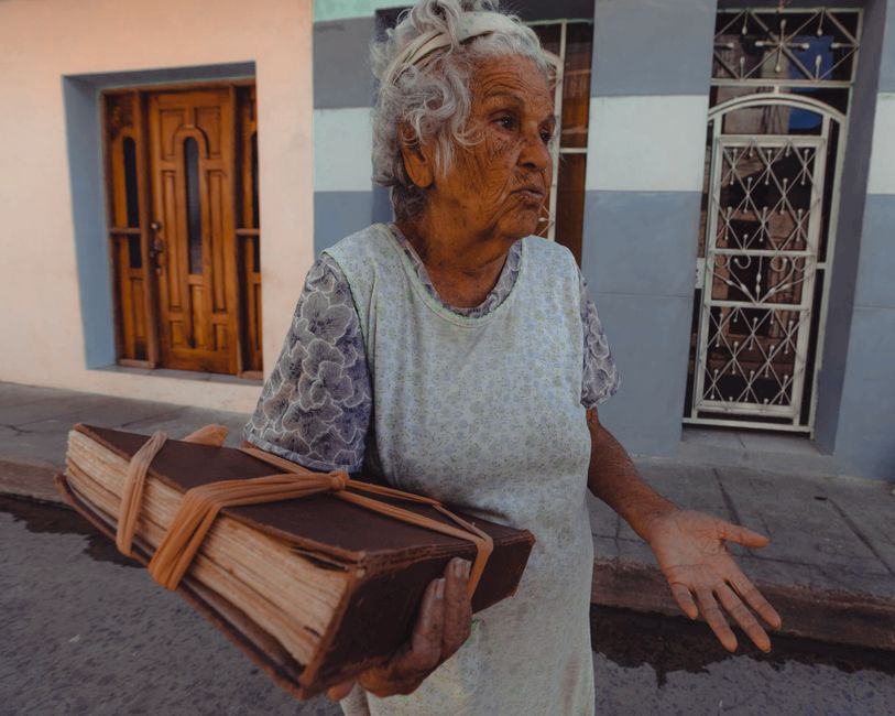 Fotomural Una mujer anciana está de pie en la calle sosteniendo un gran libro histórico, transmitiendo sabiduría y relatos.