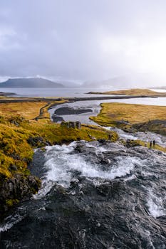 Breathtaking view of a waterfall flowing into a fjord in Iceland with moody skies.