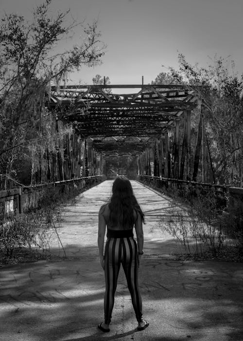 Back View Shot of a Woman Standing on a Bridge Between Trees