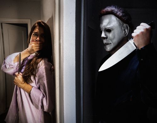 Free Dramatic horror scene featuring a masked figure and frightened woman indoors. Stock Photo