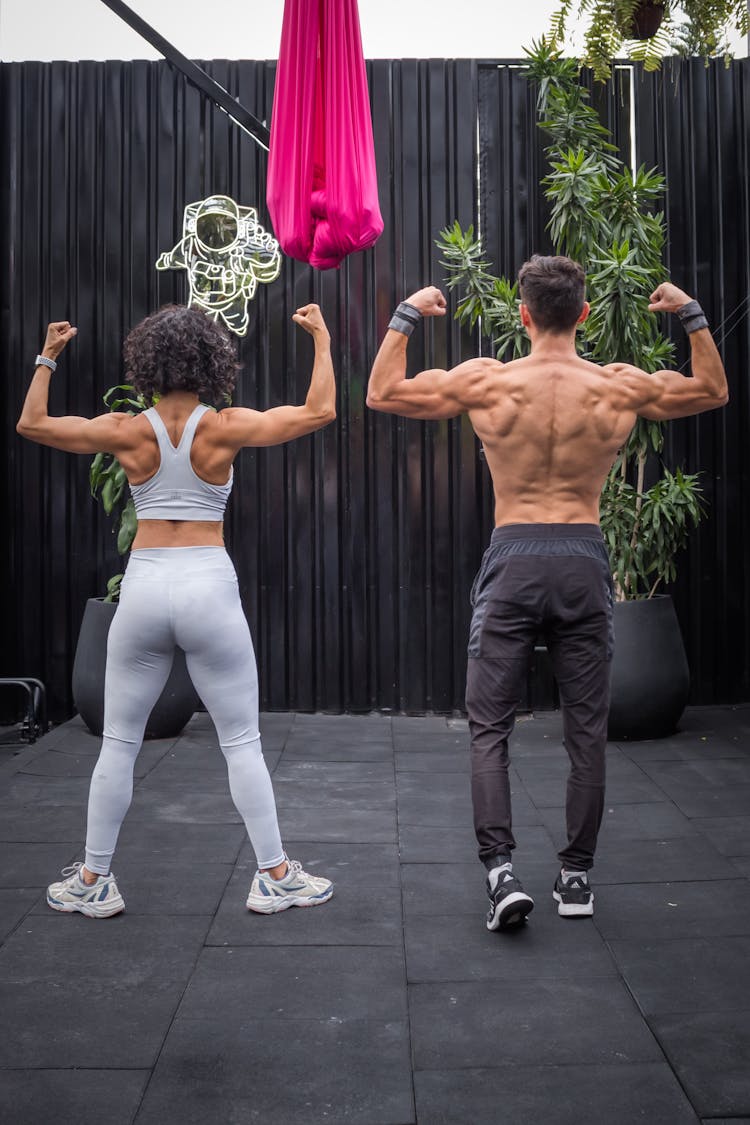 Man And Woman In Sportswear Exercising And Flexing Muscles