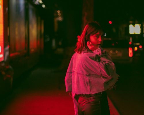 Free A young woman in a denim jacket walks through a vibrant street at night in Mexico City. Stock Photo