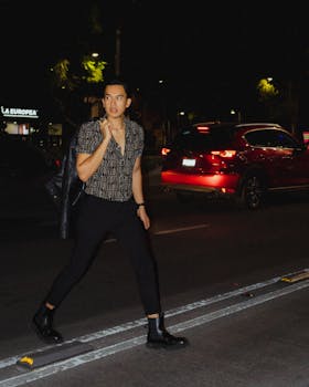 A stylish man in black attire crossing a lit street in Mexico City at night.