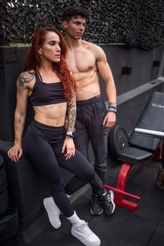 Muscular man and woman posing confidently in a gym, showcasing toned physiques and tattoos.