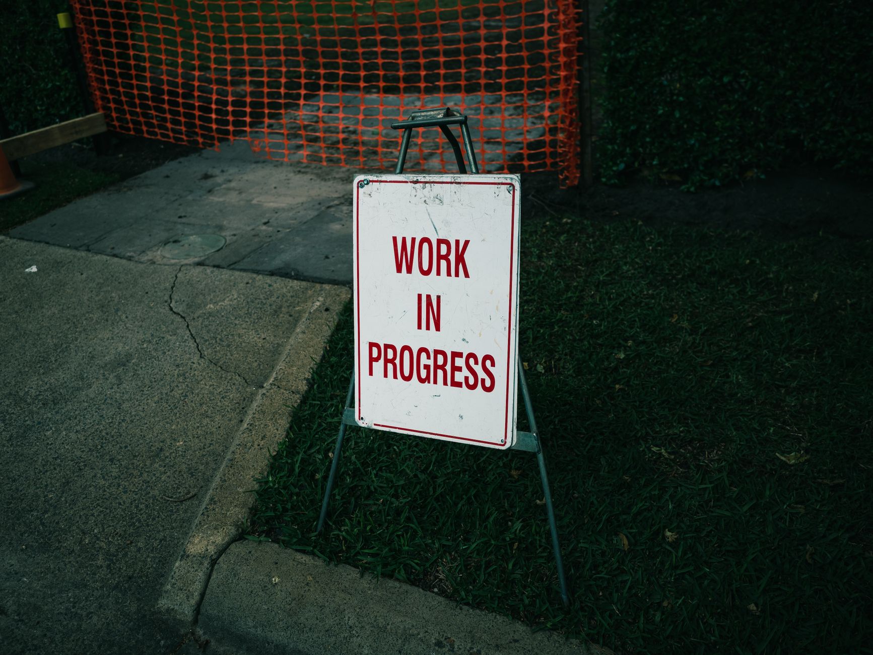 A 'Work in Progress' sign stands on a sidewalk next to safety barriers.