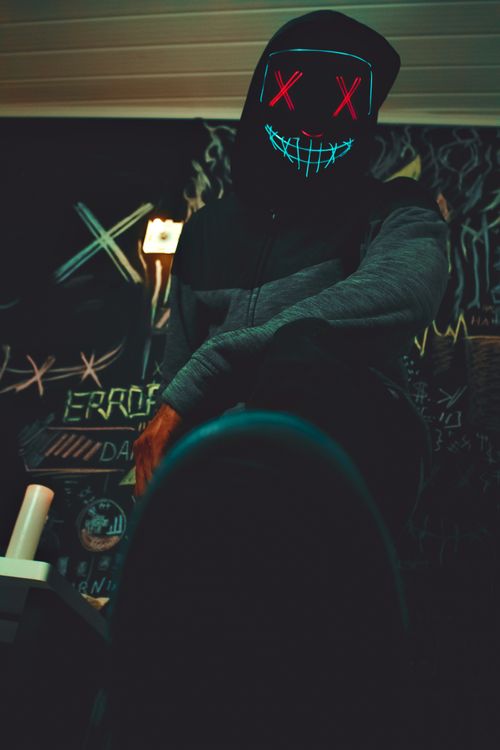 Free Mysterious figure with neon mask in dark, graffiti-filled room, creating a futuristic vibe. Stock Photo