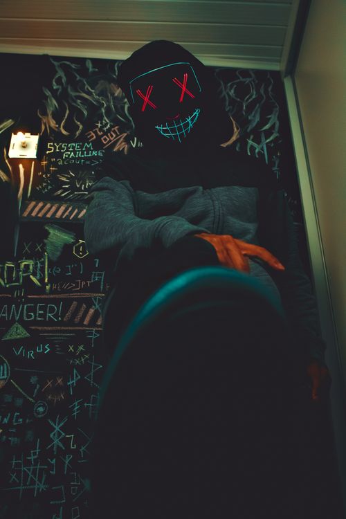 Free A mysterious figure wears a vibrant neon mask amid urban graffiti, evoking themes of anonymity and rebellion. Stock Photo