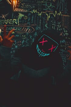Dark hooded figure with a glowing neon mask, surrounded by eccentric graffiti.