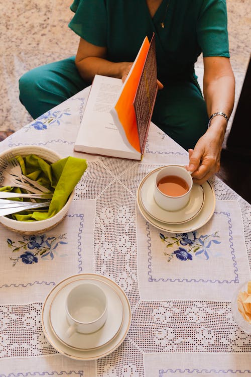 A Person in Green Shirt and Pants Holding White Ceramic Cup while Sitting on the Floor