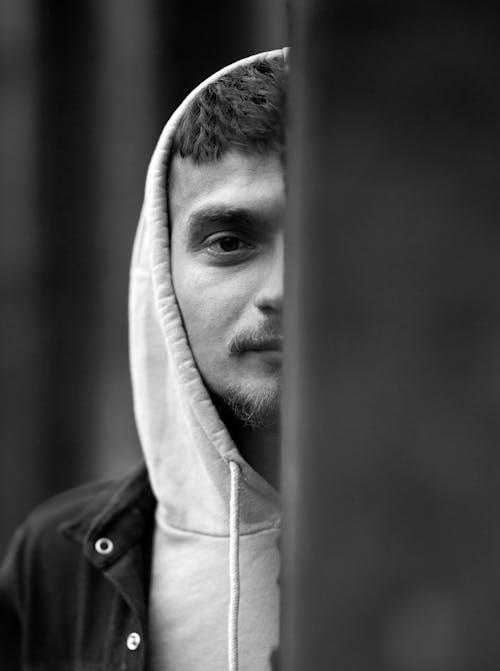 Grayscale Photography of a Man Wearing Hoodie Peeking Behind the Metal Post
