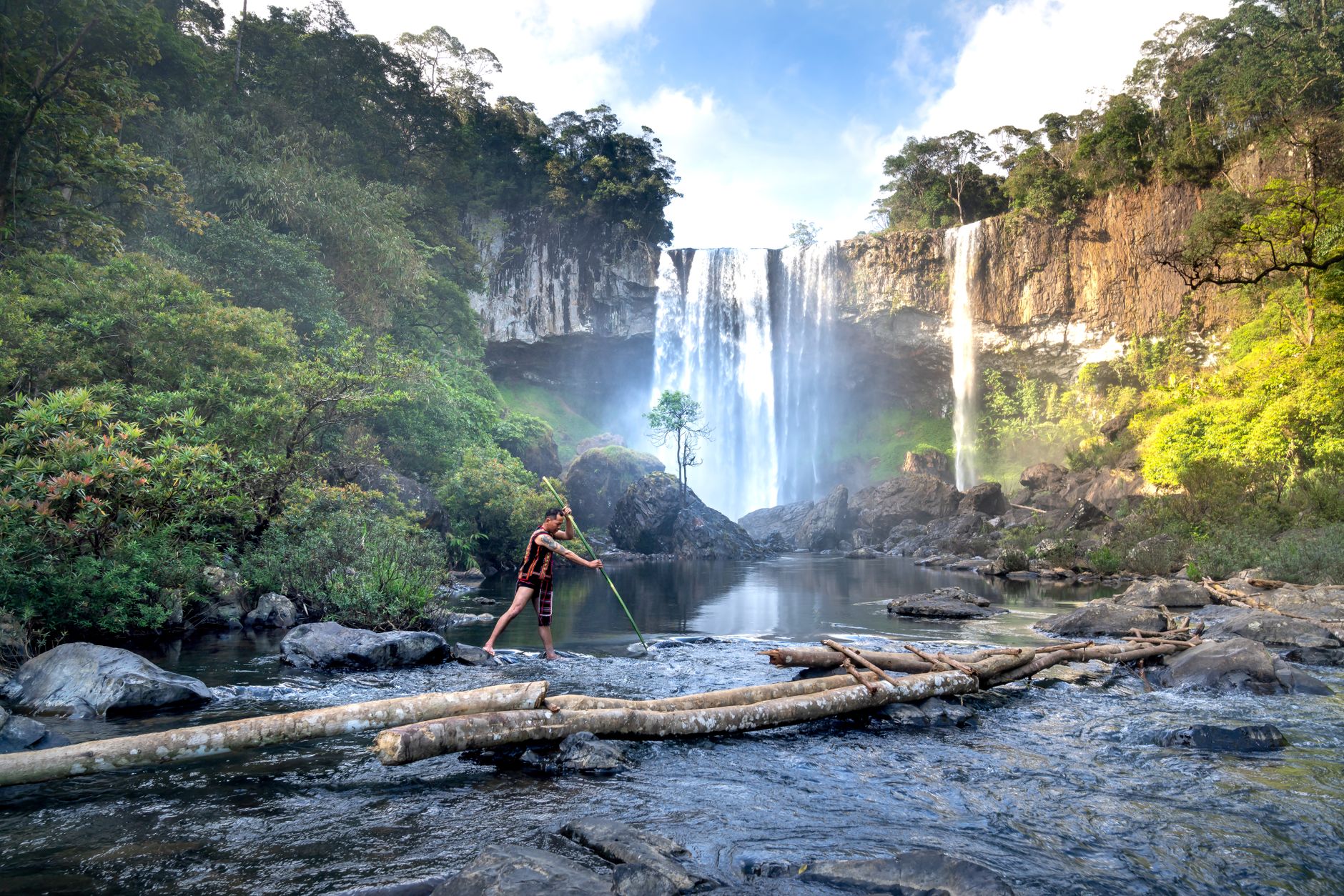 Asian man fishing with spear near waterfall in Vietnam's Kon Chu Rang Nature Reserve.