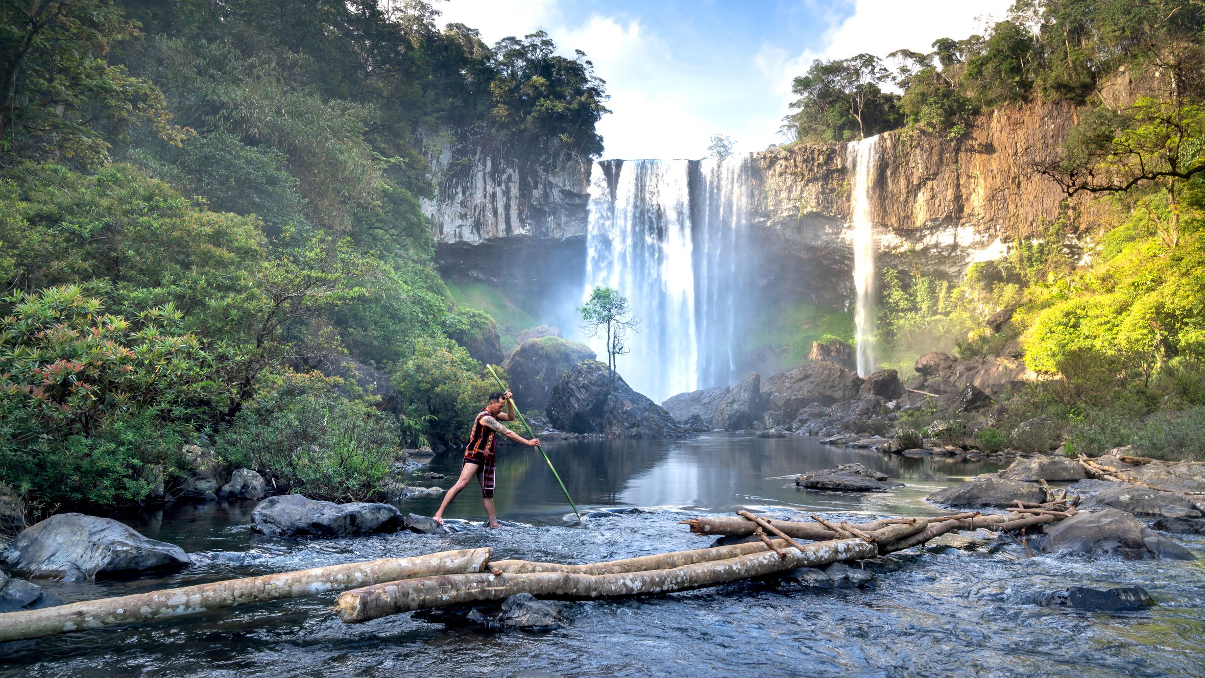 Asian man fishing with spear near waterfall in Vietnam's Kon Chu Rang Nature Reserve.