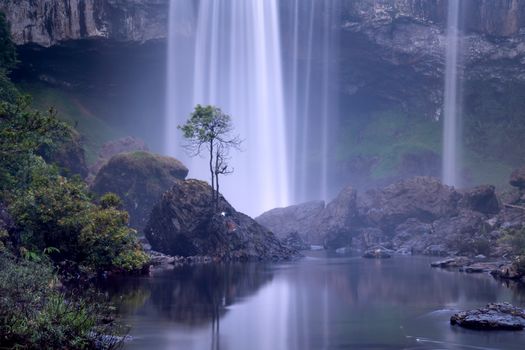 A peaceful waterfall cascading into a tranquil river surrounded by misty mountains and lush greenery.