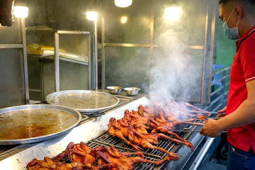 Asian vendor grilling chicken skewers, creating smoke and flavor at an outdoor stall.
