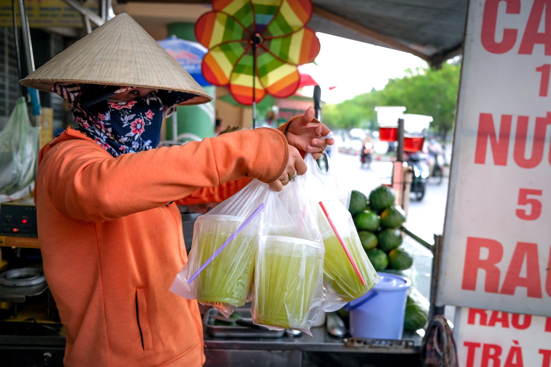 A street vendor in a conical hat selling beverages in an Asian market setting.