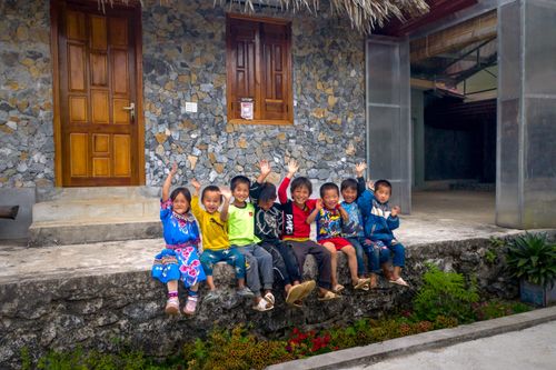 Free Group of smiling Asian children waving hands while sitting outside a residential home. Joyful and playful moment. Stock Photo
