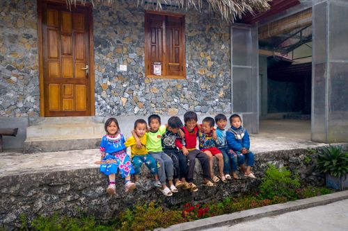 Free Cheerful group of children sitting on stone steps of a traditional village house. Stock Photo