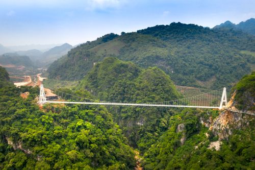 Free Aerial view of a beautiful suspension bridge spanning a lush green valley with mountainous backdrop. Stock Photo