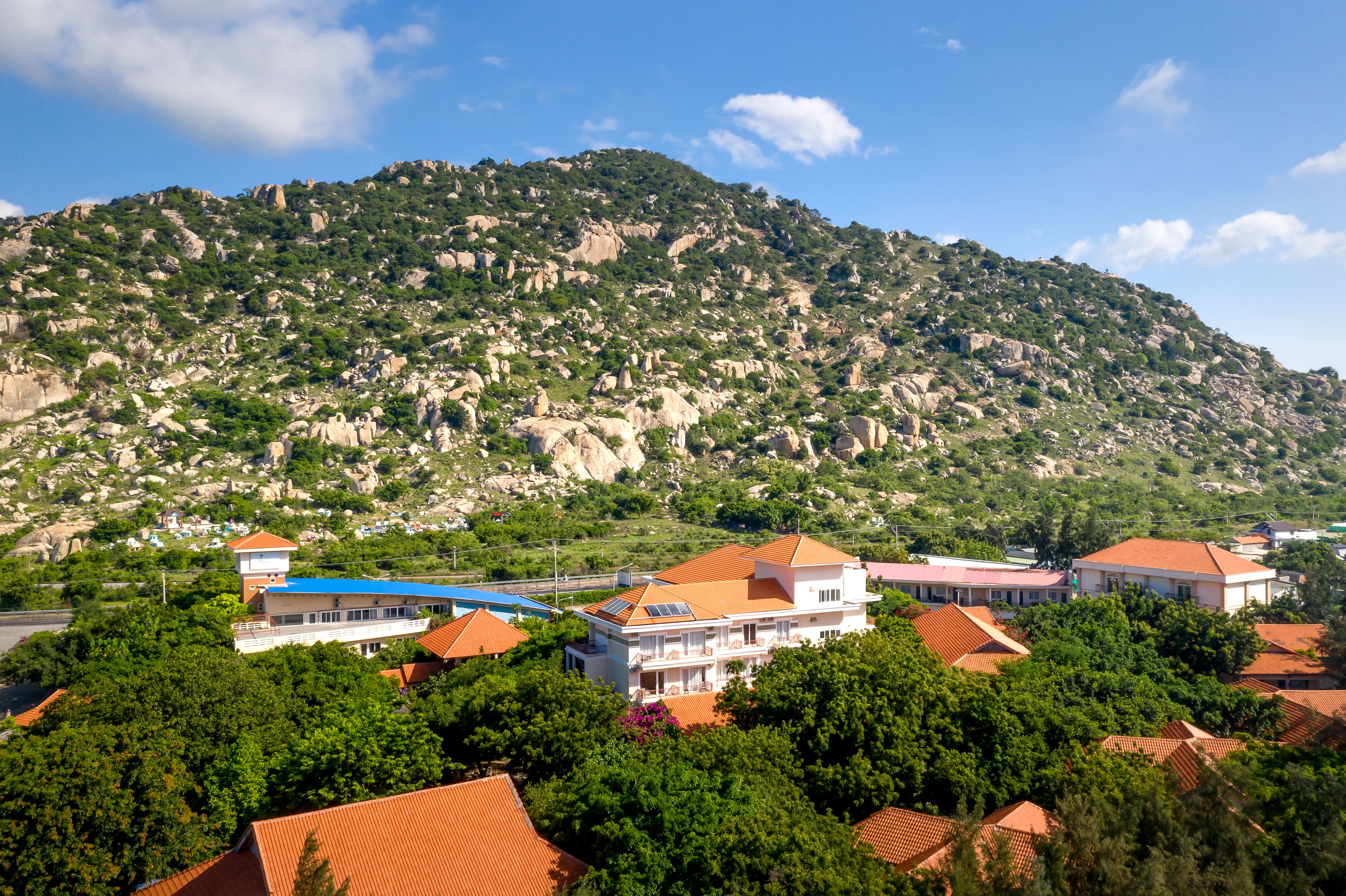 Aerial view of lush green hills surrounding Ho, with a small hotel rooftop visible