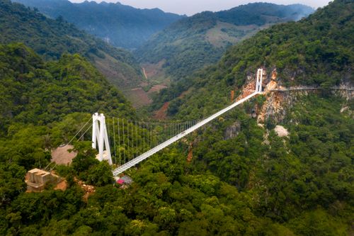 Free Stunning aerial view of a suspension bridge spanning a lush green valley surrounded by hills and mountains. Stock Photo