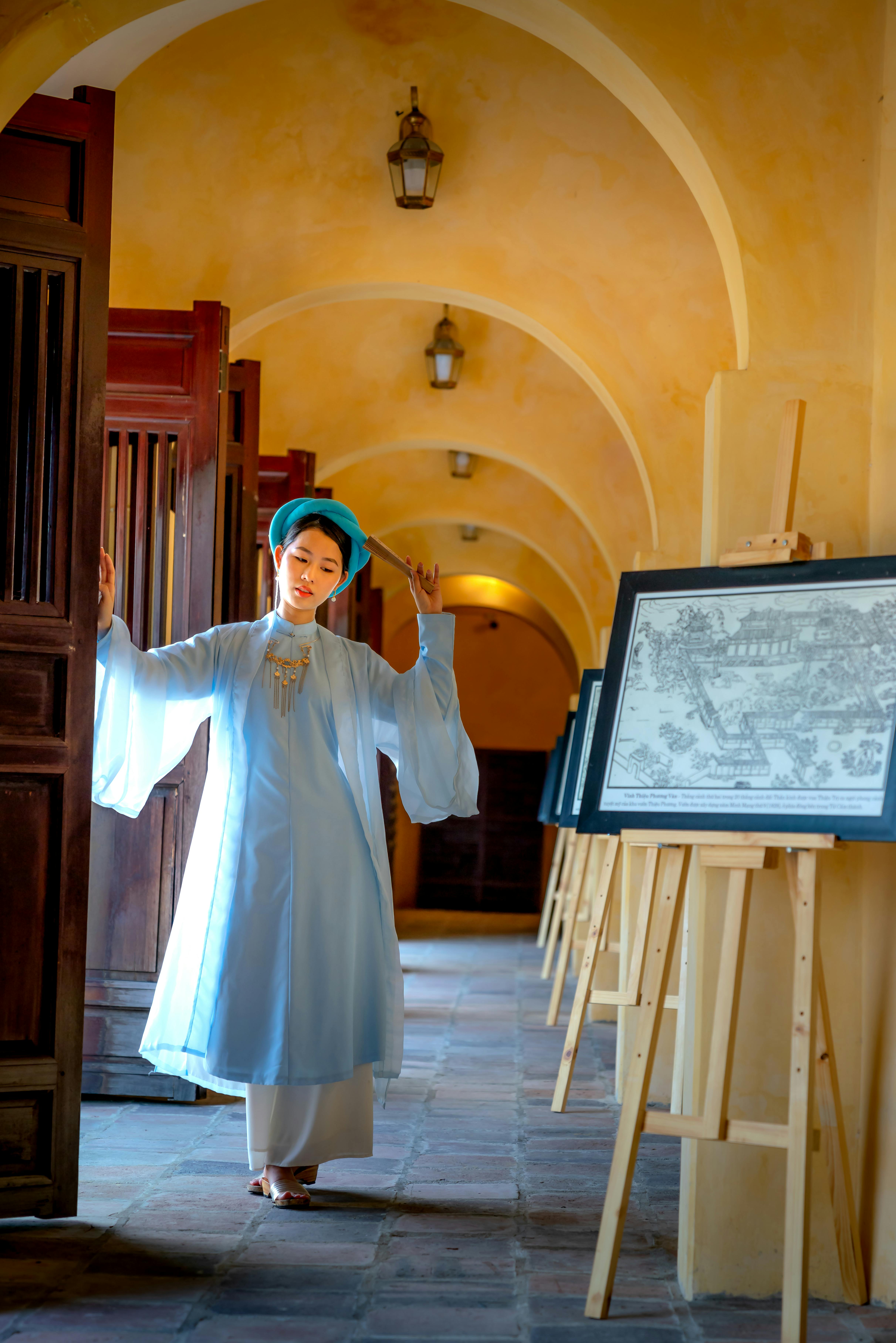 A serene woman in traditional attire gracefully poses in a beautifully lit museum corridor.