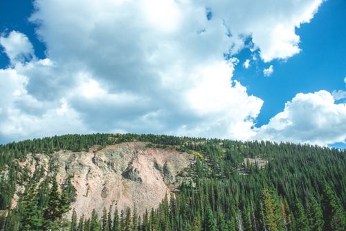Free Breathtaking view of a lush green hillside with a clear blue sky and fluffy clouds. Stock Photo