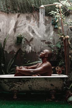 African American man enjoying a refreshing shower in an outdoor bathtub surrounded by greenery.
