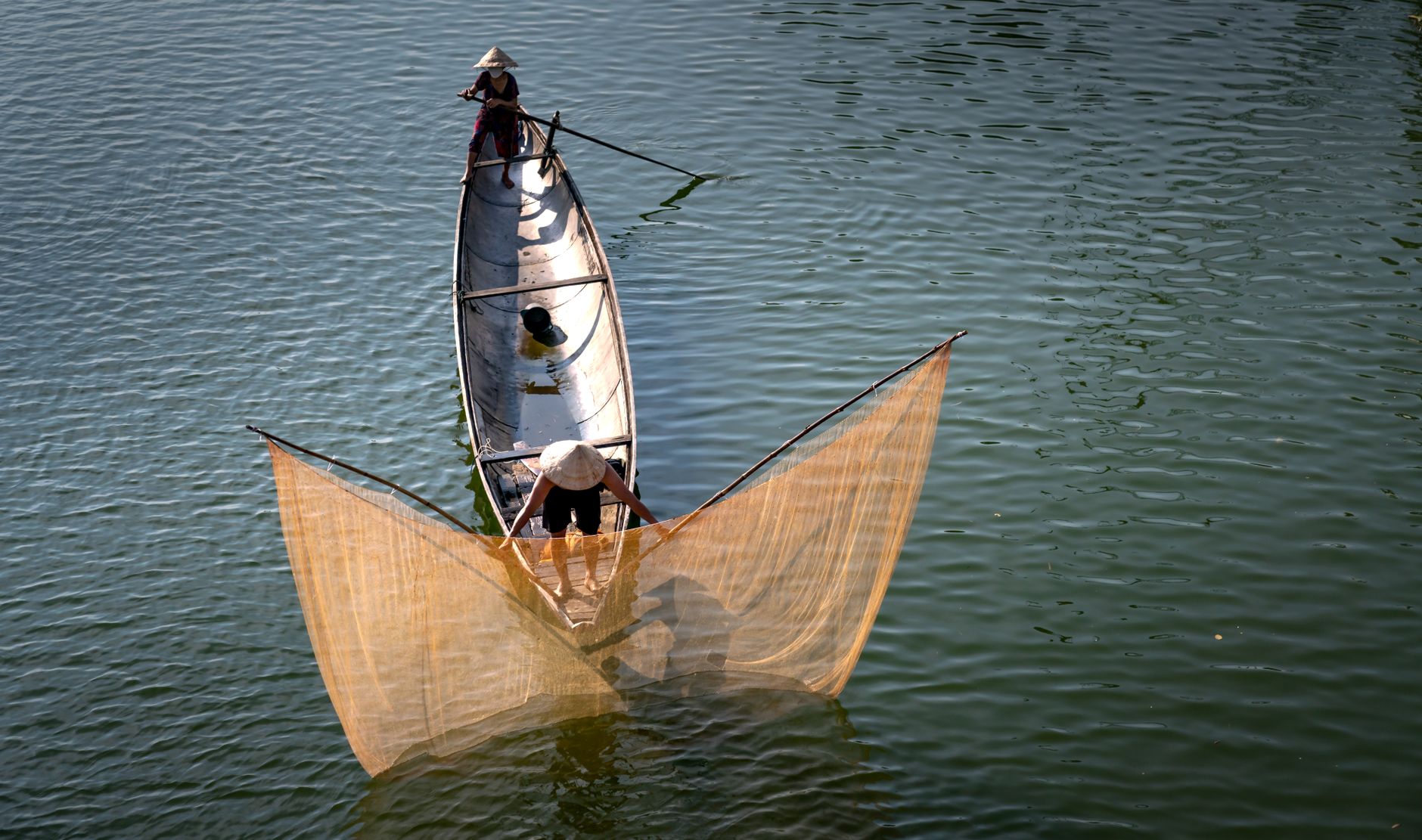 Fishermen on a boat casting nets in a calm river, showcasing traditional fishing techniques.