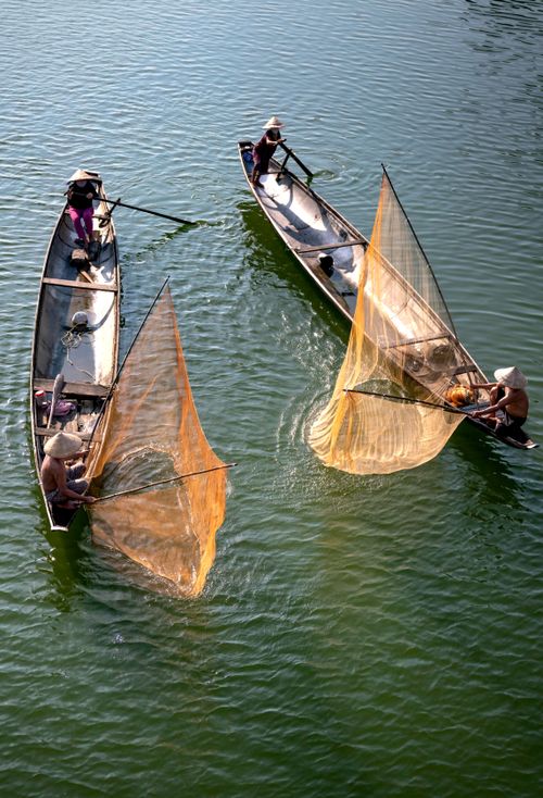 Free High-angle view of fishermen using conical nets on boats in a calm river. Stock Photo